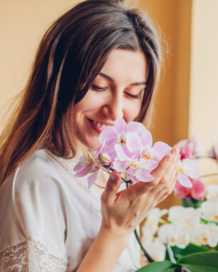 Happy woman smelling blooming purple orchid holding pot. Girl gardener taking care of home plants and flowers.